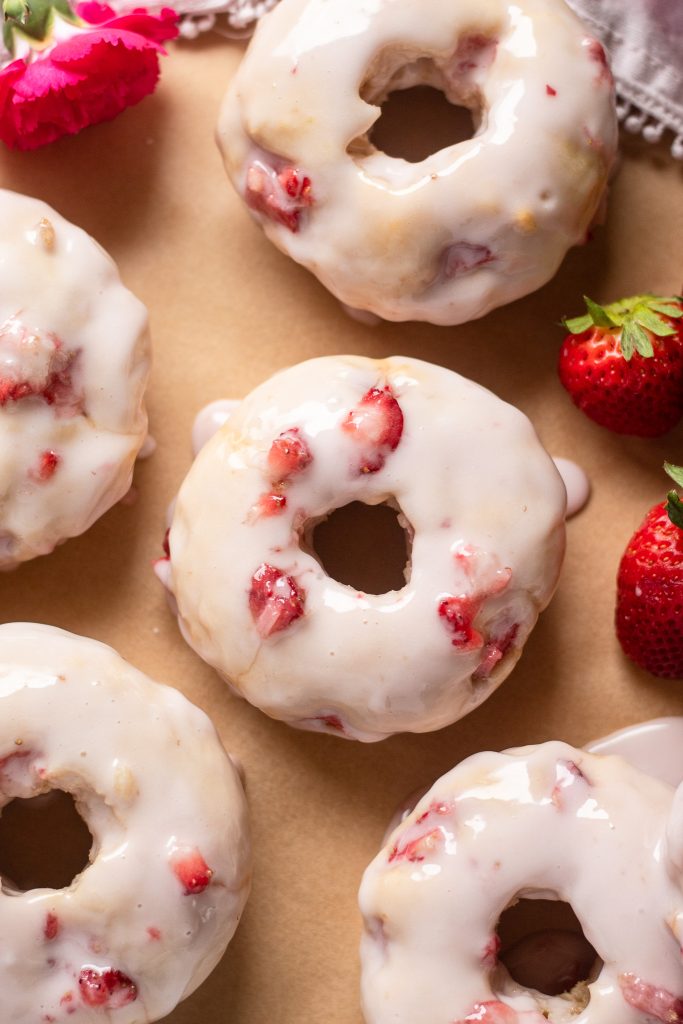 overhead photo of strawberry elderflower glazed donuts with pink flowers and strawberries in photo