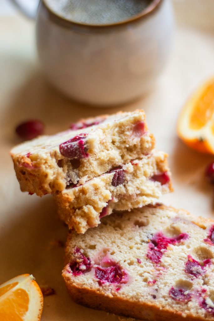 close up of inside of a slice of cranberry orange bread with a cup of coffee in the background